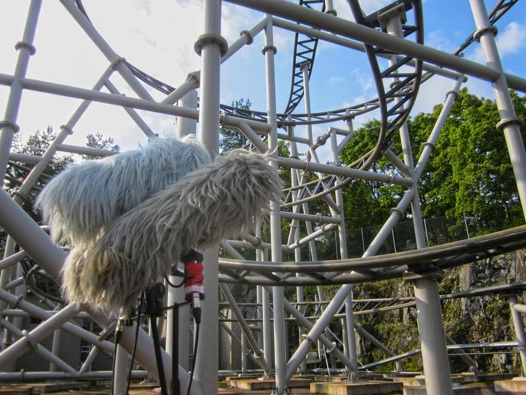 Two boom mics are set up beneath a twisting roller coaster track