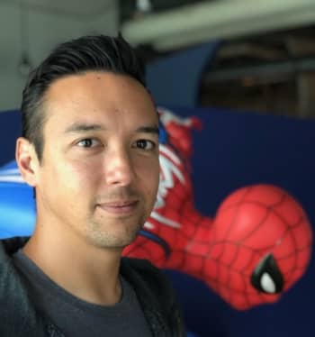 A man with black hair smiles gently near a Spider-Man statue.