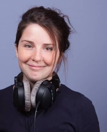A woman with headphones around her neck smiles.
