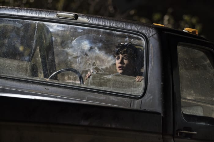 A boy sits in the backseat of an old truck with wide eyes looking through the back window.