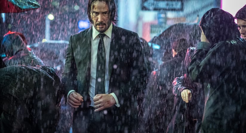 John Wick walks through a dark city as rain pours