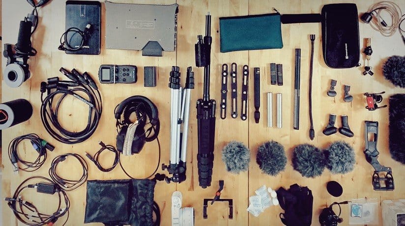 A plethora of gear including mics, windscreens, cables, an interface, a pair of headphones, and a hard drive.