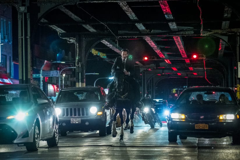 John Wick races under the above-ground subway on a horse with a motorcyclist behind him
