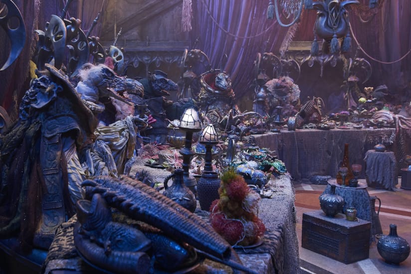 Several Skeksis gather for a meal in a dark chamber.