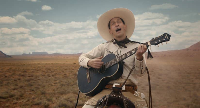 A man with a guitar and a white hat sings in the Montana desert.