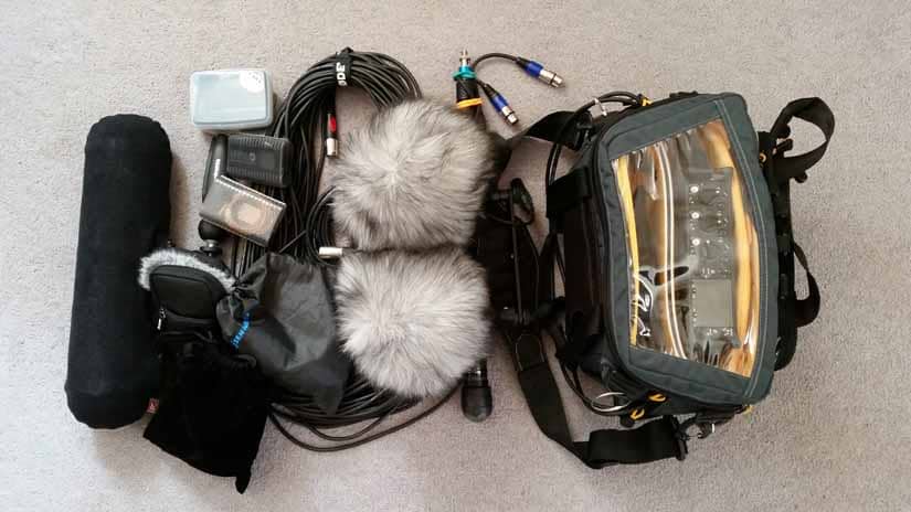 An assortment of mics, cords, muffs, and a digital recorder in a bag sit together