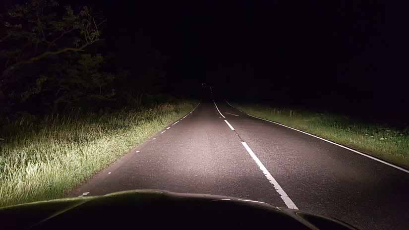 Headlights shine on a Scottish road and into a pitch black night