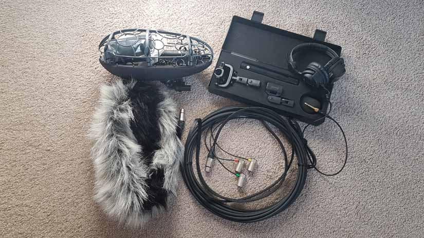 A wind screen, cords, headphones, and a box with a condenser mic sit together