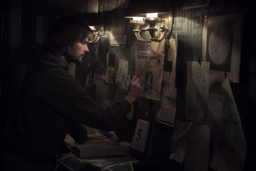 A man studies the web of newspaper clippings and drawings pinned to his wall.