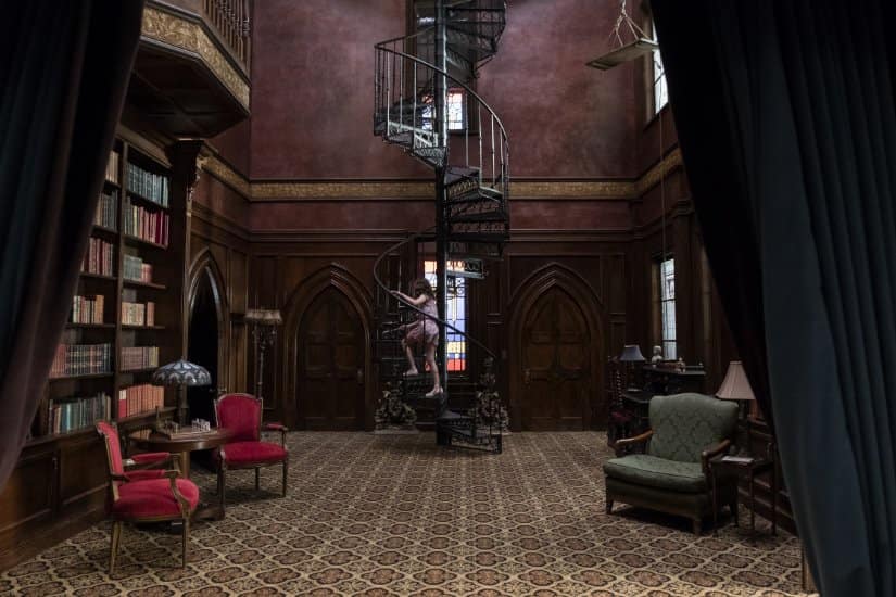 A girl walks up a spiral staircase in the mansion's library.