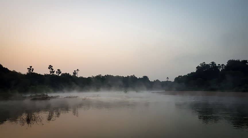 Light fog floats above a river at dawn.