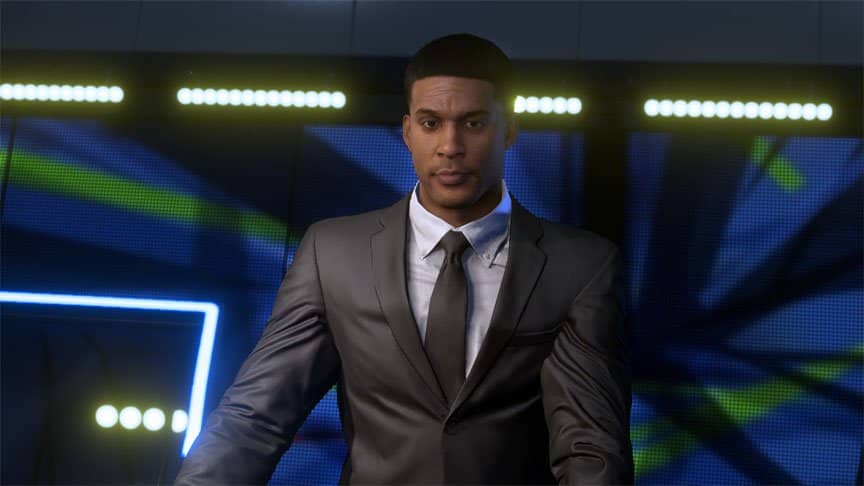 Devin Wade stands tall in front of a screen wearing a chic, dark grey suit.