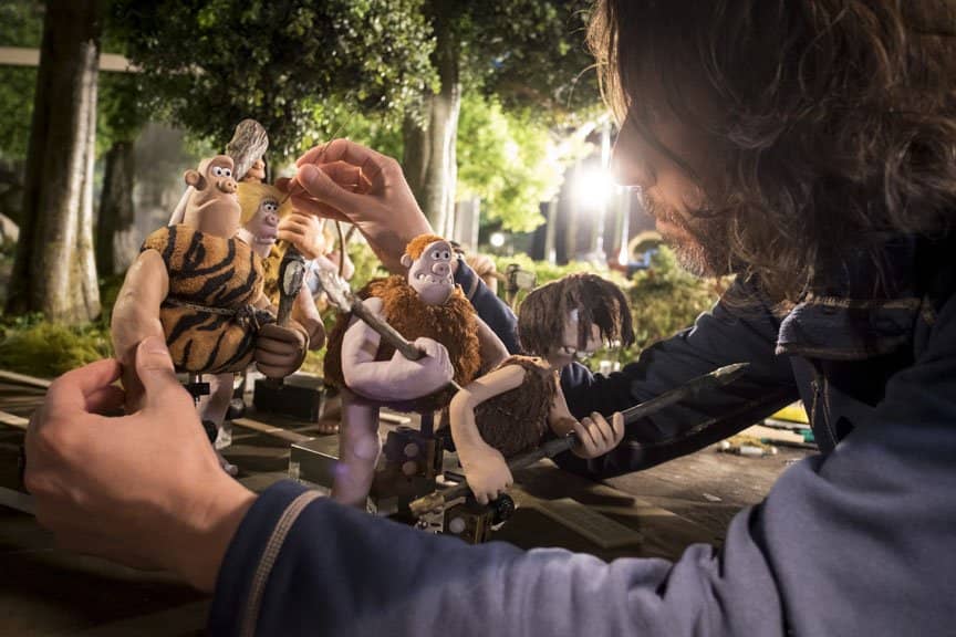 A man configures the caveman characters in a stop motion animation scene.