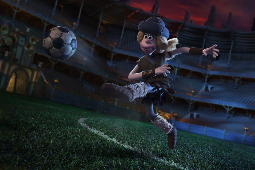 A woman in furry pelts kicks a football in a massive stadium.