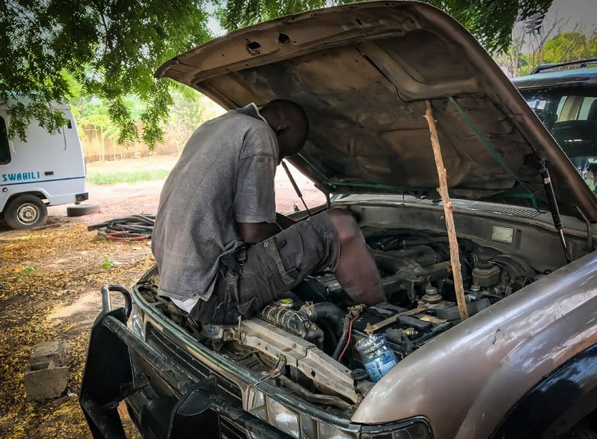 A mechanic sits under the hood of the car working.