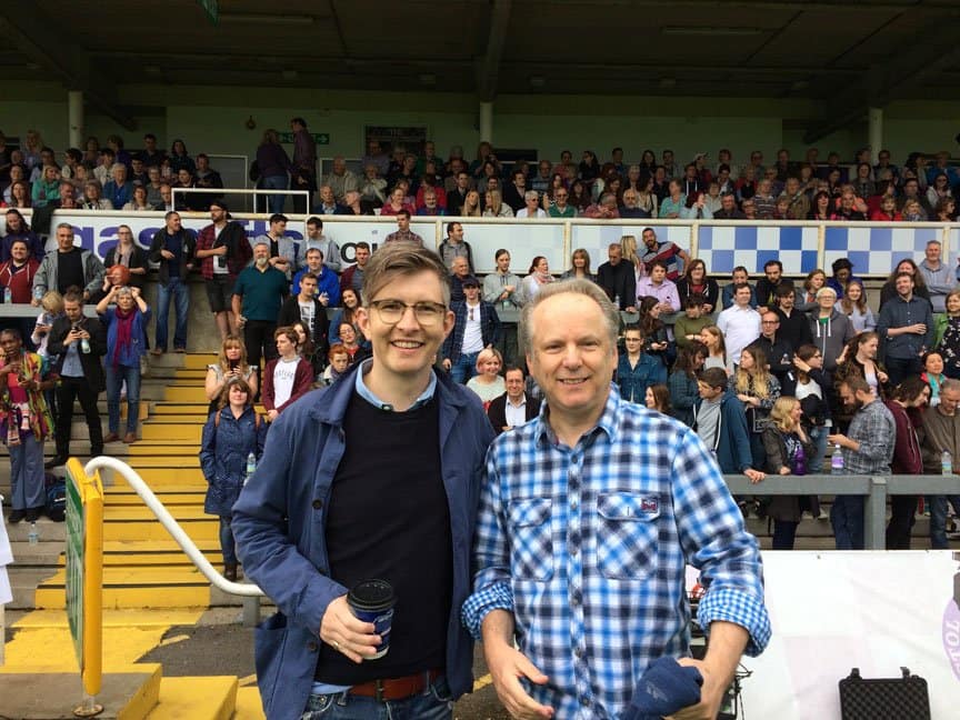 Two men stand in a stadium packed with people.