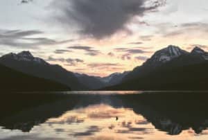 The dusk sky reflects in a calm lake outlined by moutains