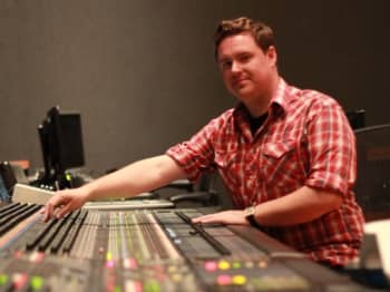 A man controls mixing console while looking at the camera
