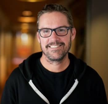 A man with glasses and a brown beard wearing a hoodie.