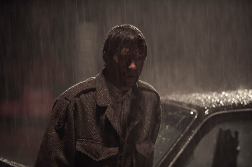 A bloodied man exits a crashed car.