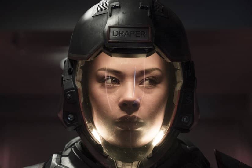 A woman wears a spacesuit with a bottom lit helmet.
