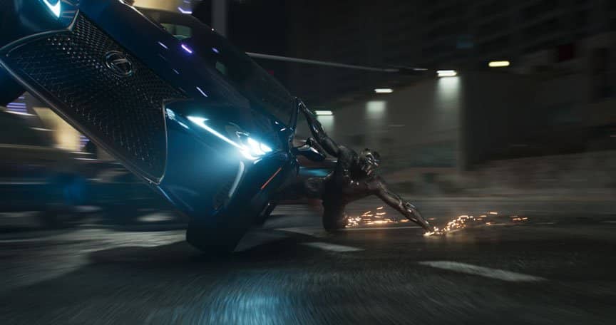 Black Panther hangs off the side of a car, sparks flying where his claws meet the road.